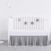 Biloban gray pleated crib skirt with pompoms adds soft texture and tidy edge.