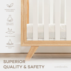 Crib with white bars and natural wood legs by Comfy Cubs in a cozy nursery