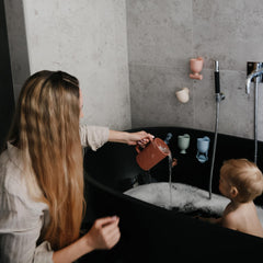 Mushie bath rinse cup demonstrates pouring action for soap and suds-free rinse.