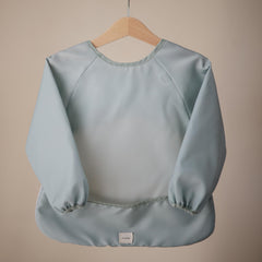 Mushie long sleeve bib in Roman Green shows the pocket catching crumbs during meals