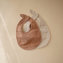 Mushie muslin bib in fog shows soft fabric for gentle coverage during feeds.
