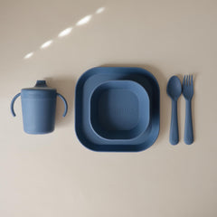 Mushie plates on table with utensils, modern calm color enhances family mealtime.