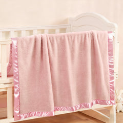 Pro Goleem crib blanket with pink satin trim keeps baby cozy in the nursery.