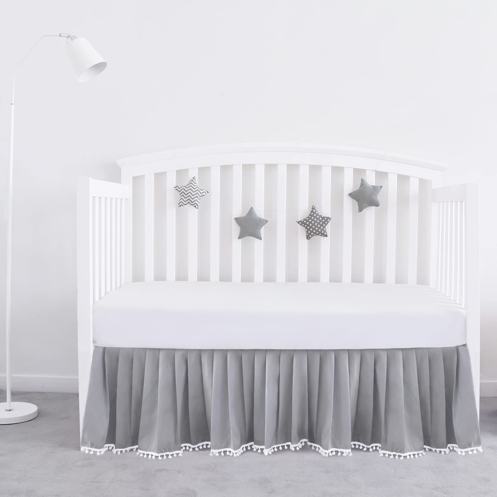 Biloban gray pleated crib skirt with pompoms adds soft texture and tidy edge.