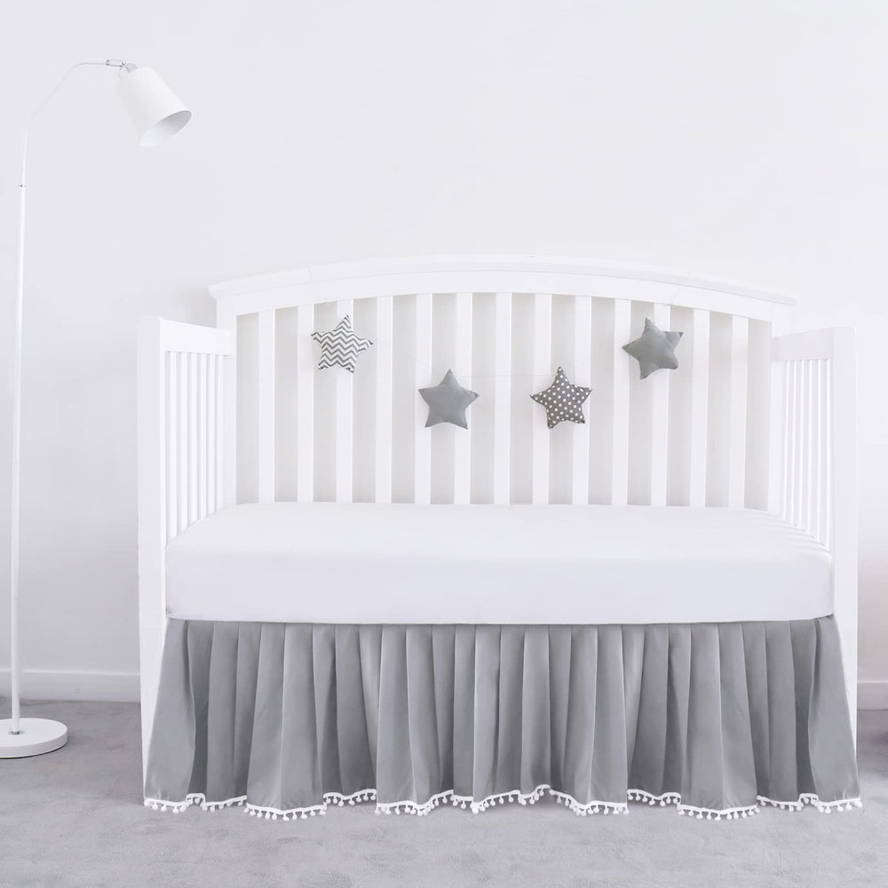 Biloban gray pleated crib skirt with pompoms adds soft texture and tidy edge.