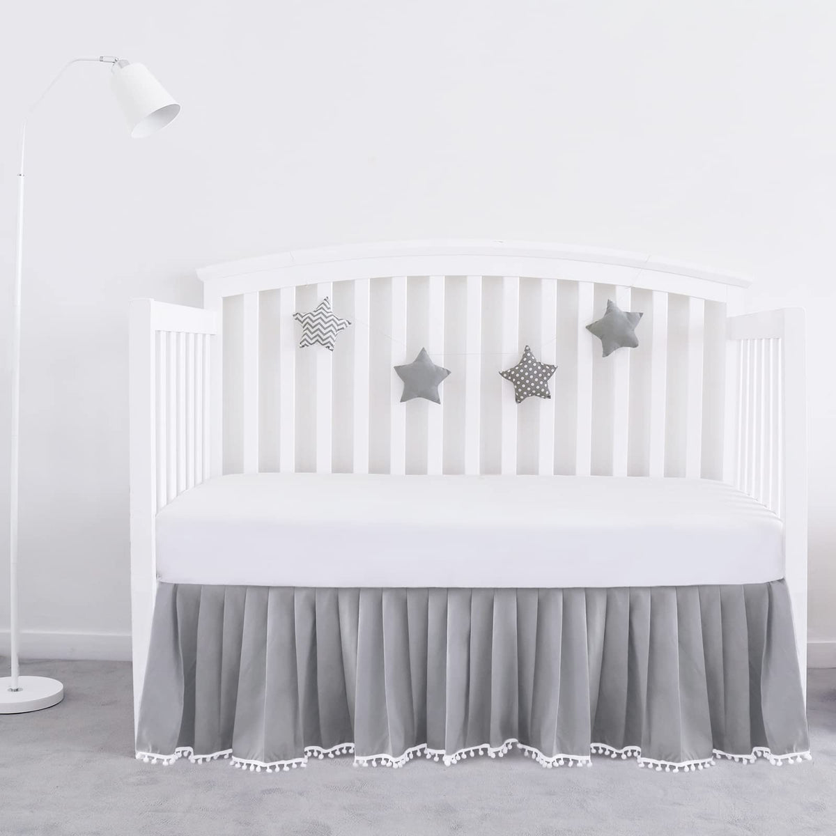 Biloban gray pleated crib skirt with pompoms adds soft texture and tidy edge.