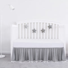 Biloban gray pleated crib skirt with pompoms adds soft texture and tidy edge.