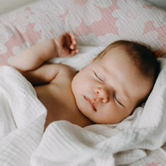 Gllquen muslin cotton sheets laid out on a bassinet bed.
