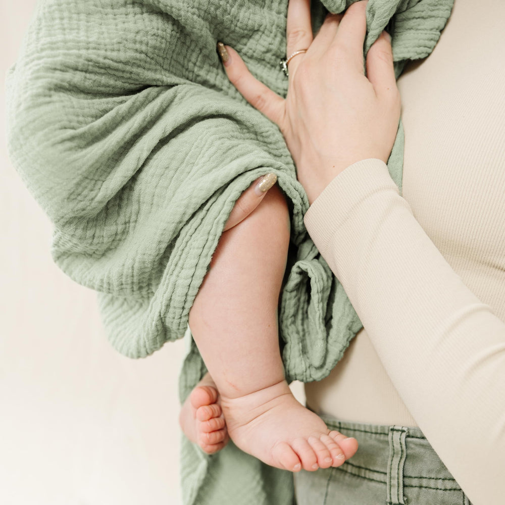 Newborn wrapped snugly with Konssy muslin swaddle in Woodland Sage color.