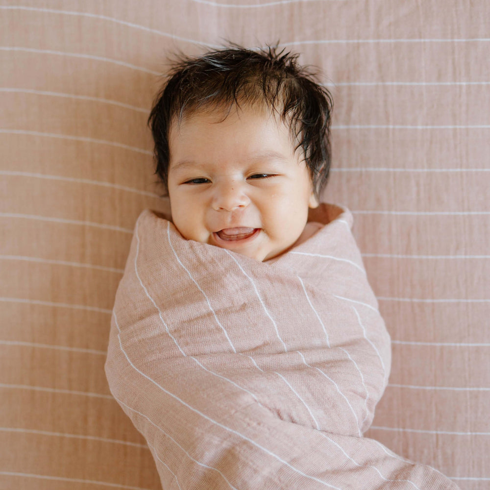 Little Unicorn Mauve Stripe swaddle being machine washed for easy care.