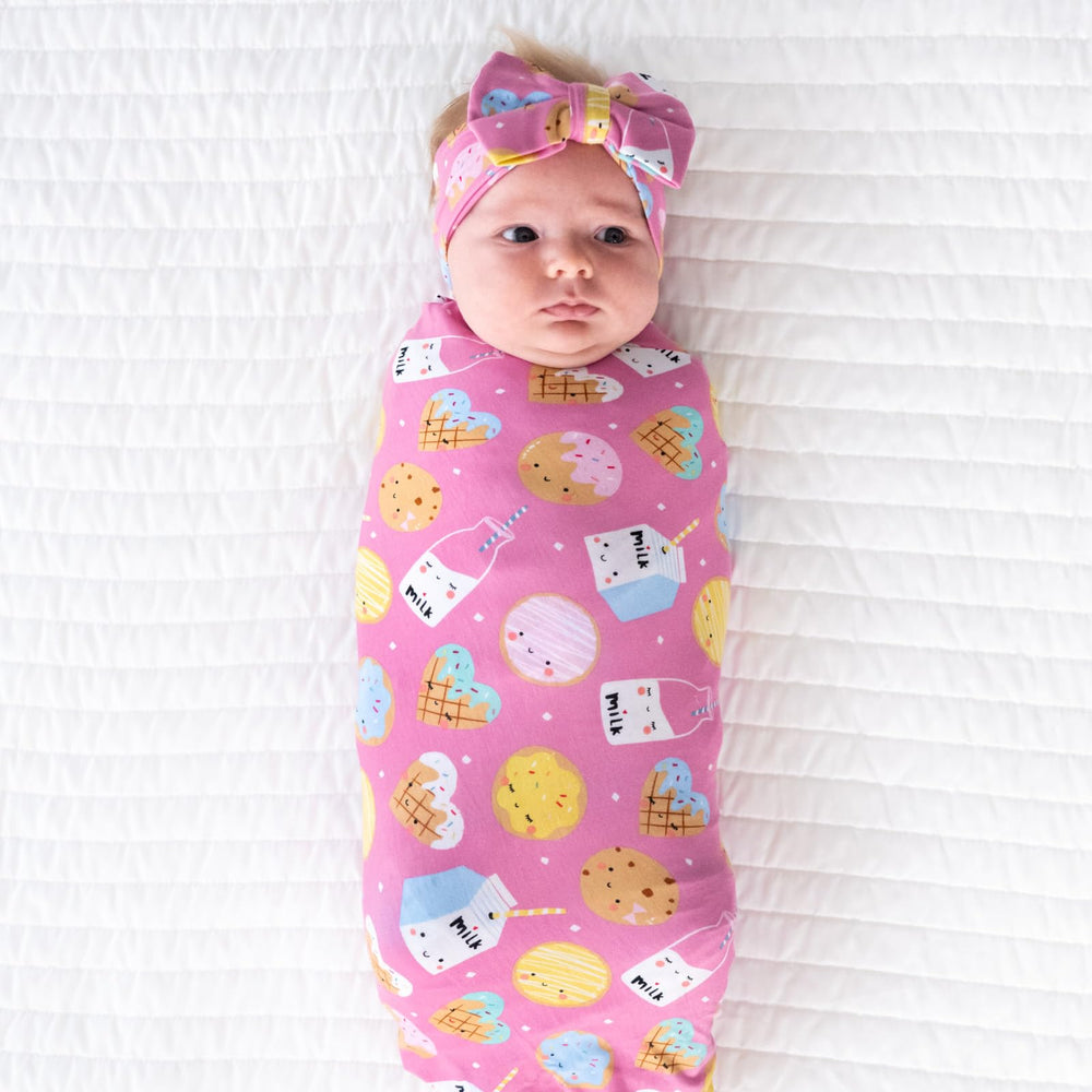 Little Sleepies swaddle blanket laid flat in pink cookies & milk pattern for cozy swaddling.