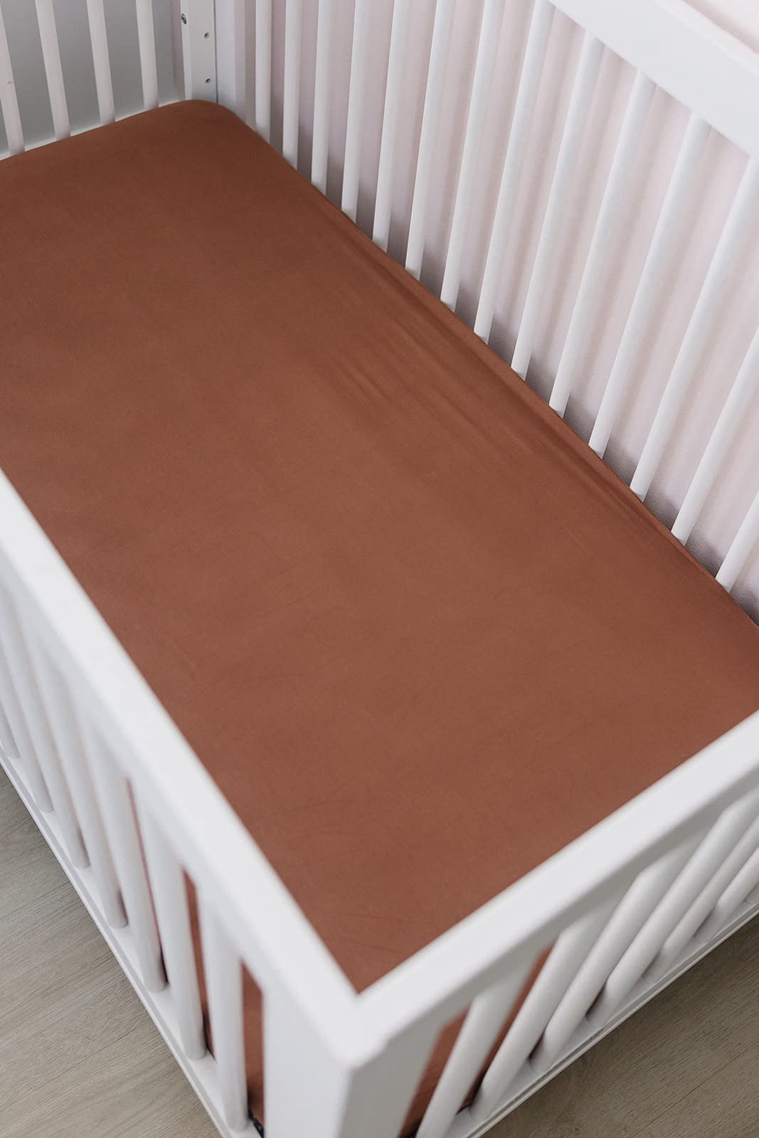 Mebie Baby stretch sheet rust on bed demonstrates secure, stretch-to-fit design.
