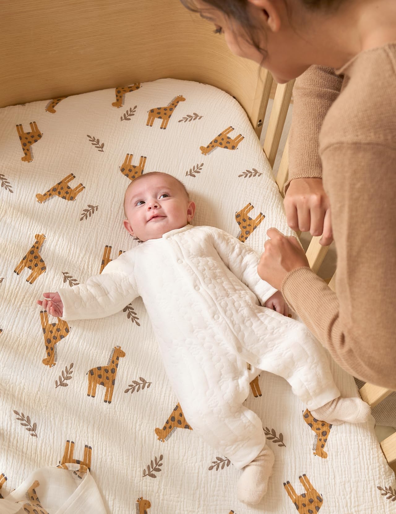 Momcozy Bravery Giraffe in a baby bed scene showing a smooth sleeping surface.