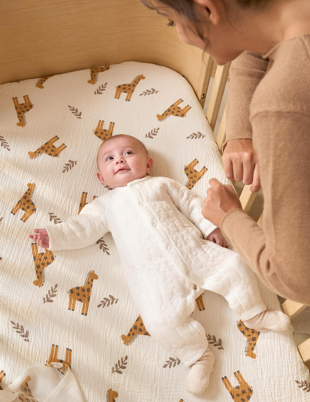Momcozy Bravery Giraffe in a baby bed scene showing a smooth sleeping surface.