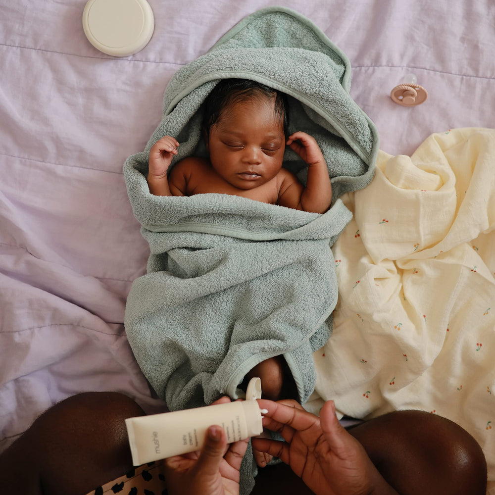 Mushie baby hooded towel Sea Mist on baby, soft drying from head to toe.