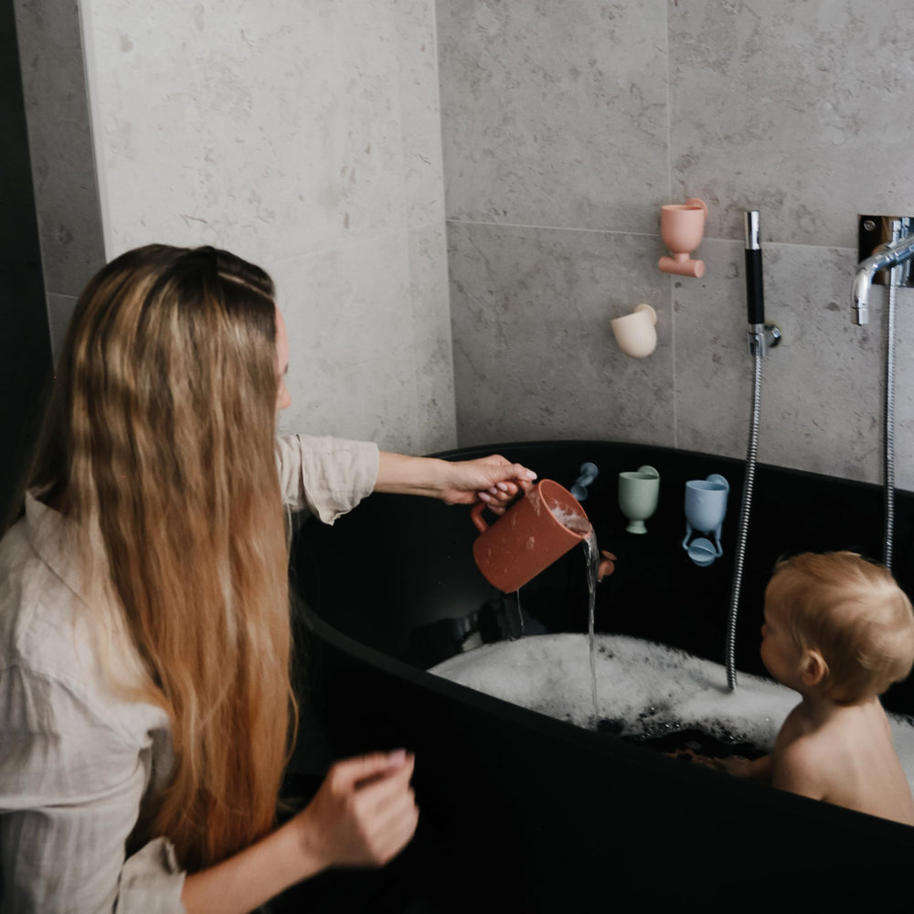 Mushie bath rinse cup demonstrates pouring action for soap and suds-free rinse.