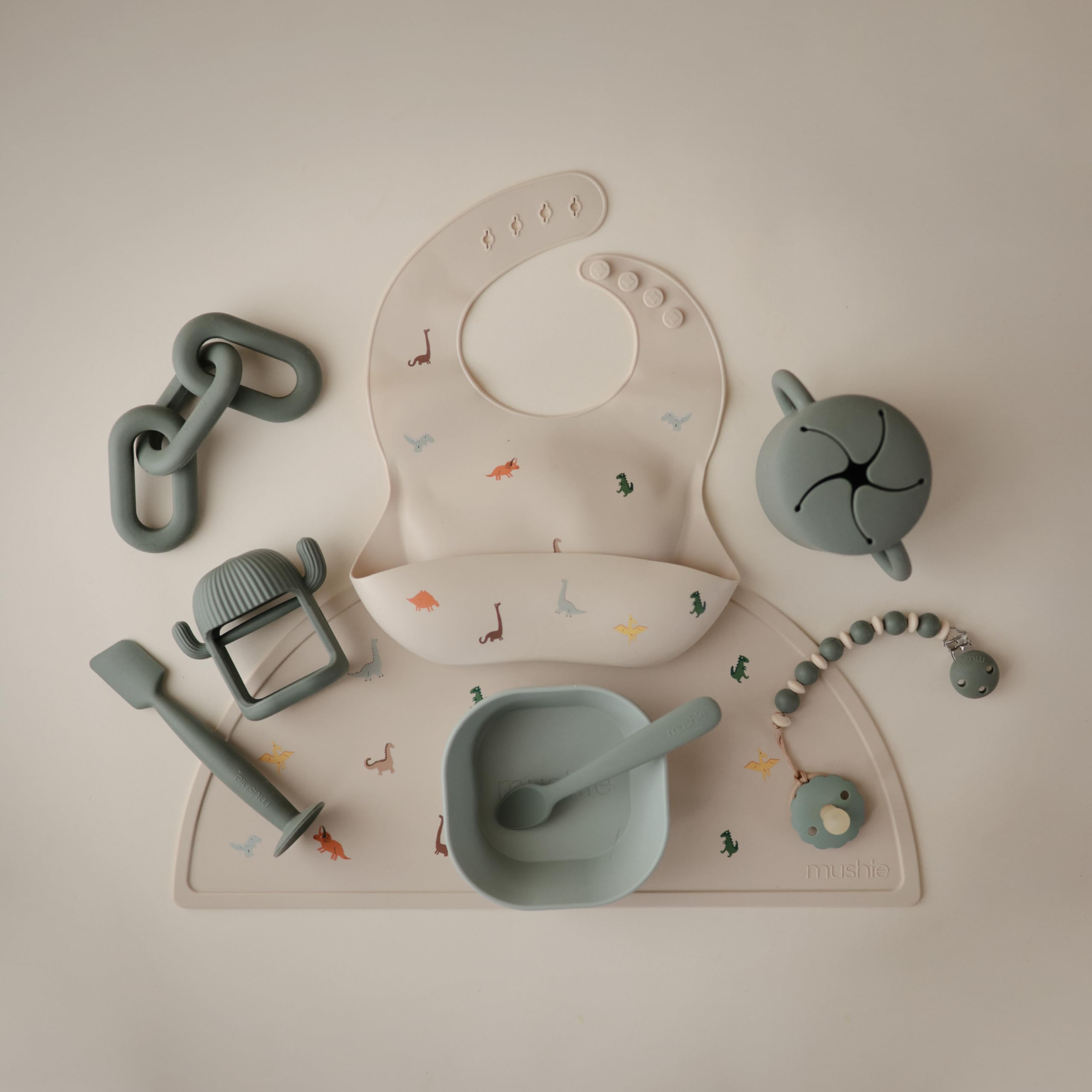 Mushie dinosaur bib pairs with placemats and tableware for meals.