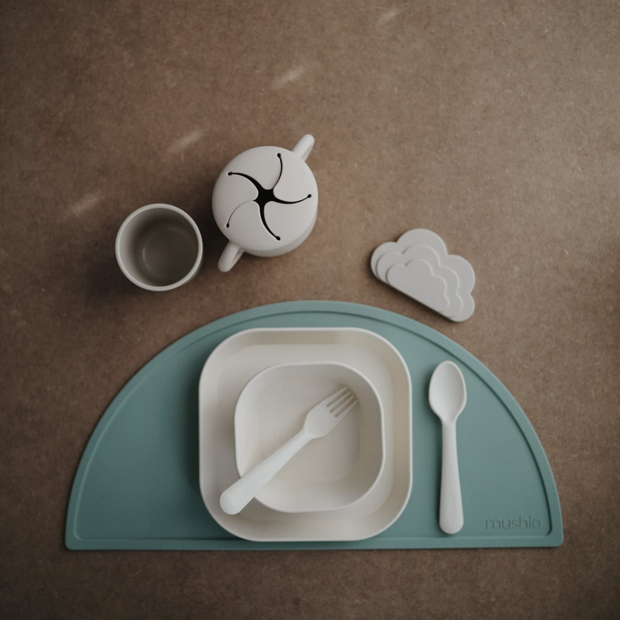 Mushie kids flatware ivory fork held by small hands.