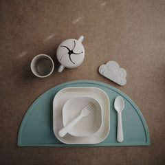 Mushie kids flatware ivory fork held by small hands.