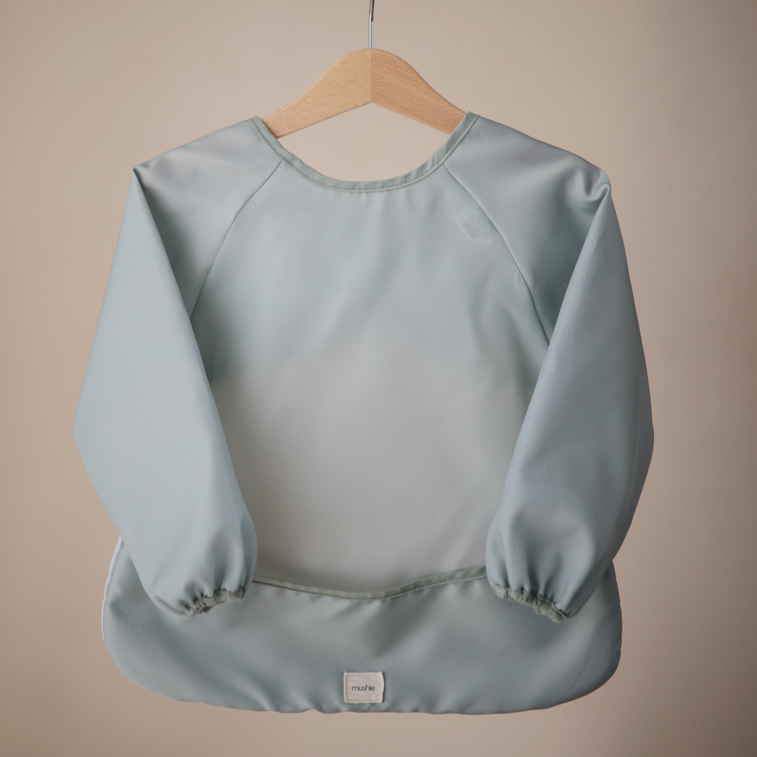 Mushie long sleeve bib in Roman Green shows the pocket catching crumbs during meals