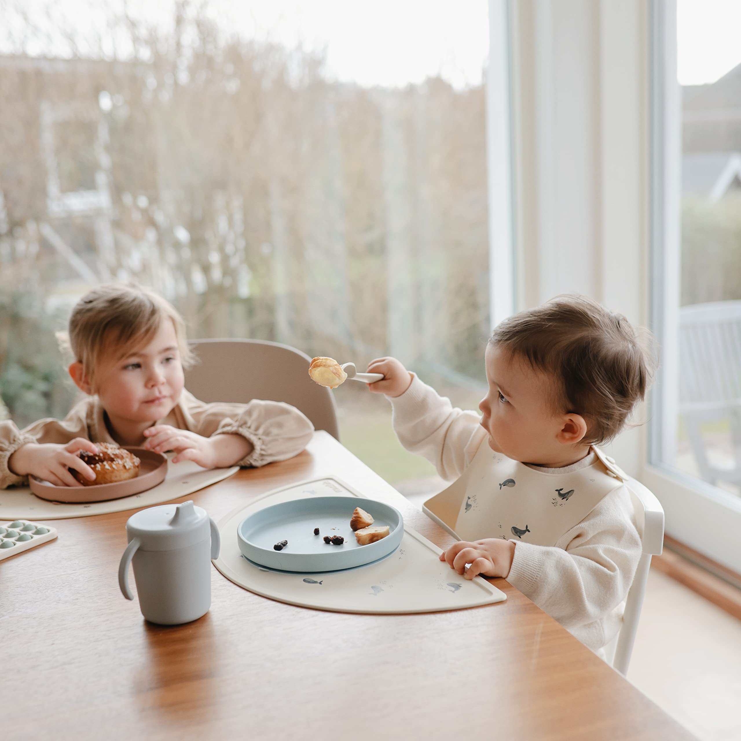 Mushie deep-front-pocket bib catches crumbs for cleaner tables and outfits.