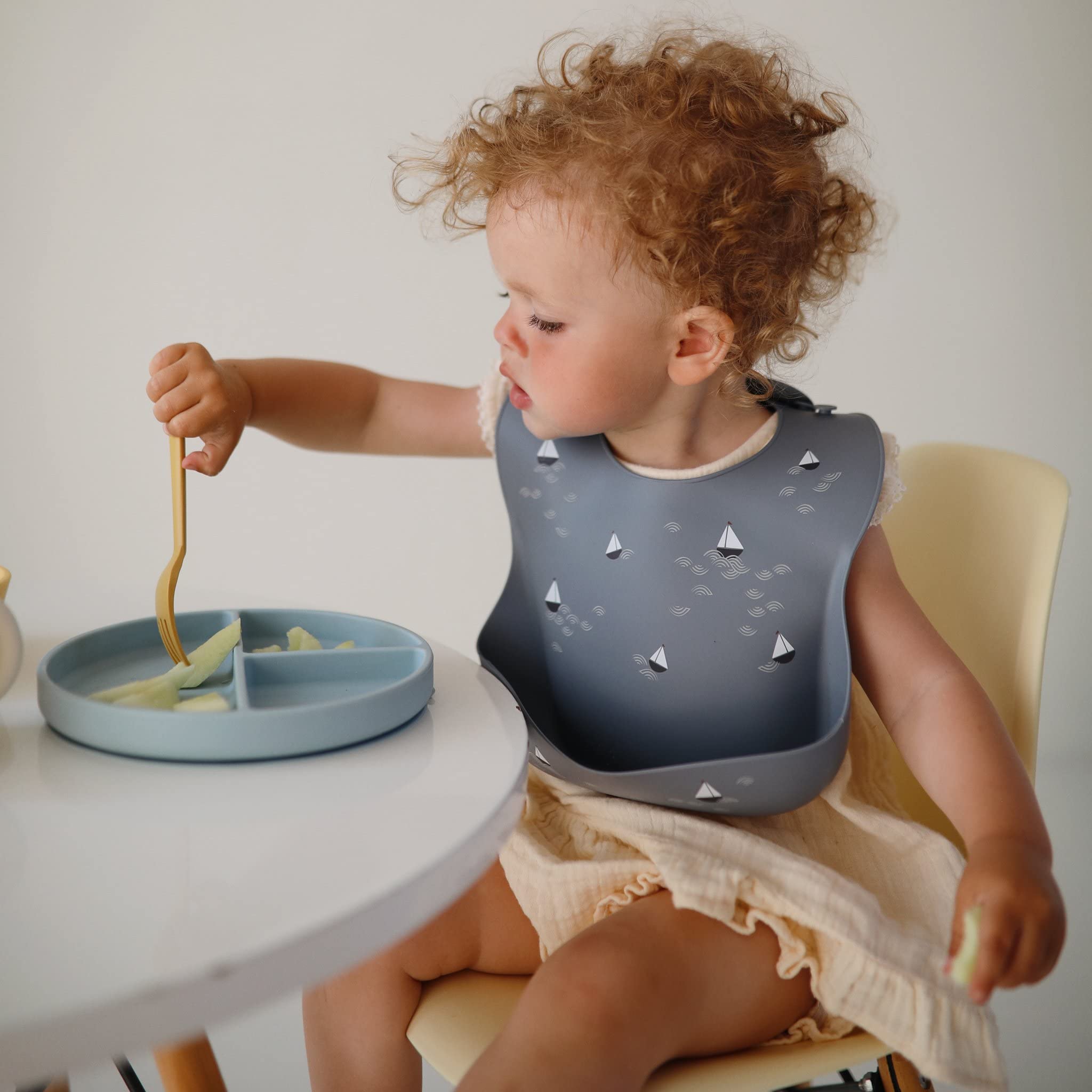 Mushie silicone baby bib deep pocket closeup, boats design, helps catch crumbs.