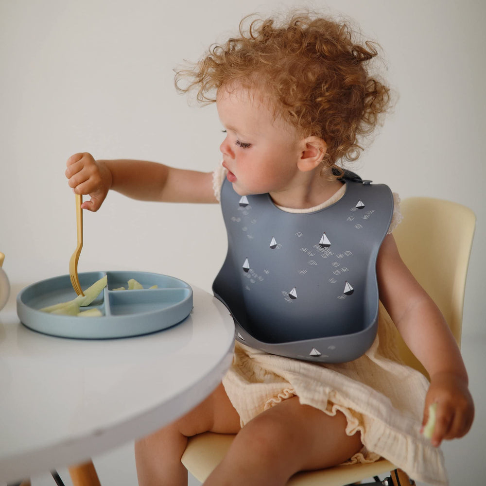 Mushie silicone baby bib deep pocket closeup, boats design, helps catch crumbs.