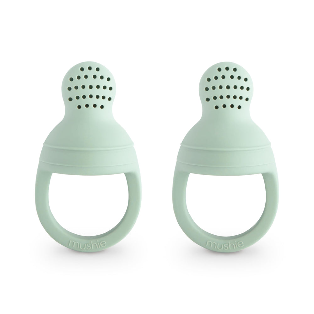 Mushie silicone baby feeder two-pack for safe self-feeding with fresh fruit.