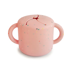 Mushie silicone snack cup with two handles helps toddler grip during on-the-go snacking.