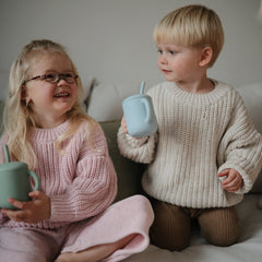 Toddler hands hold Mushie cup, supporting early motor skills.