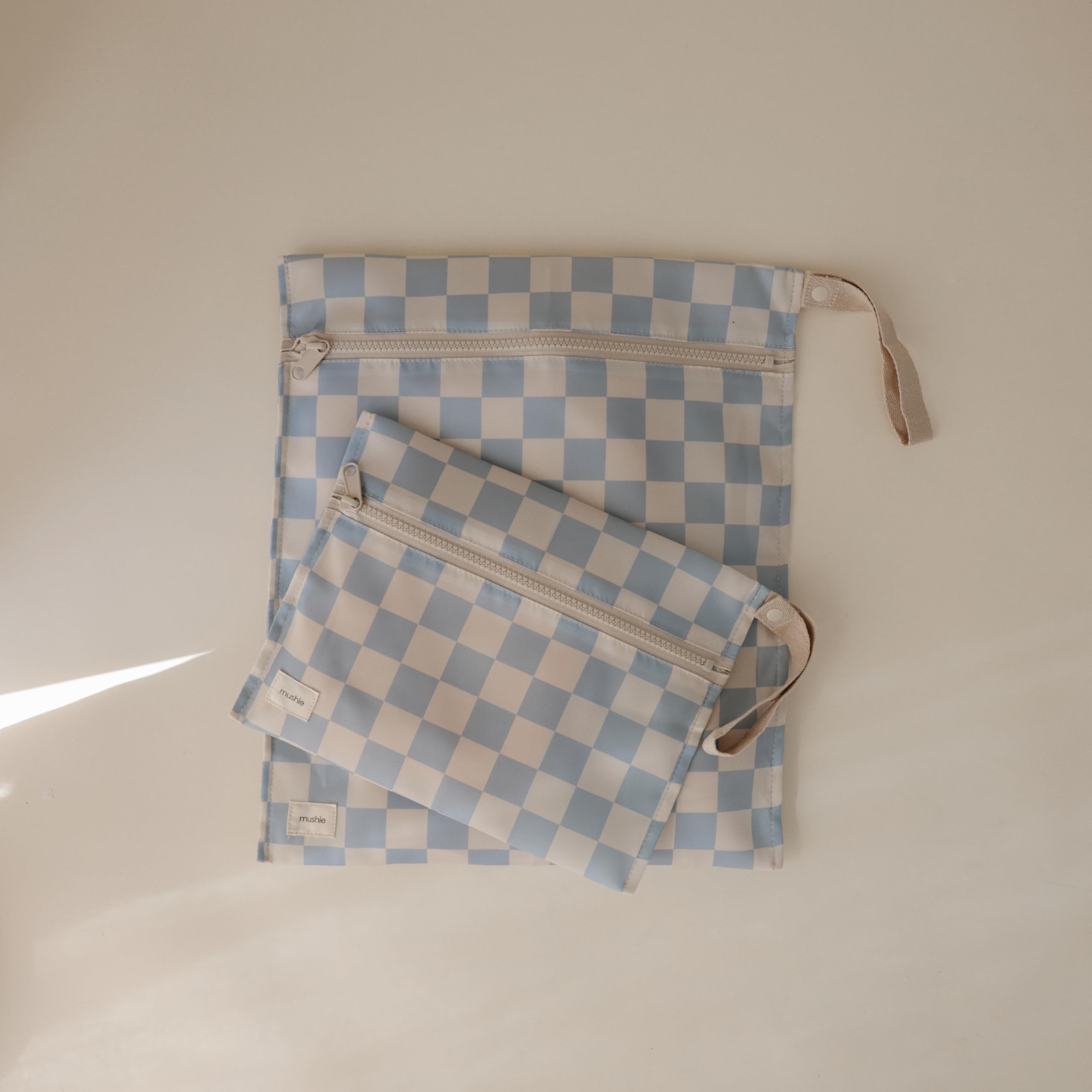Mushie wet bag blue-check with handle and snap for stroller attachment.