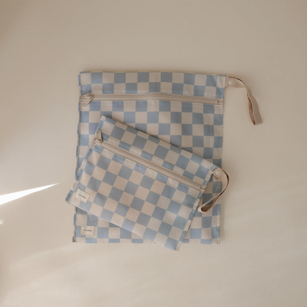 Mushie wet bag blue-check with handle and snap for stroller attachment.