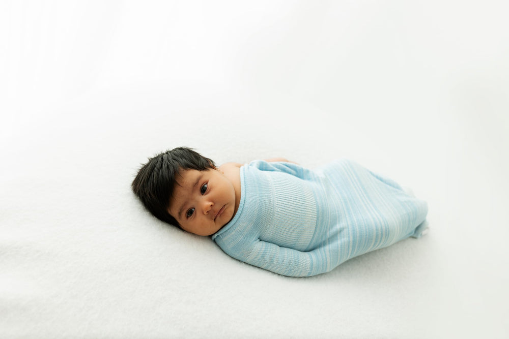 Baby in blue Swaddelini sleep sack asleep, supported by Hug Technology.