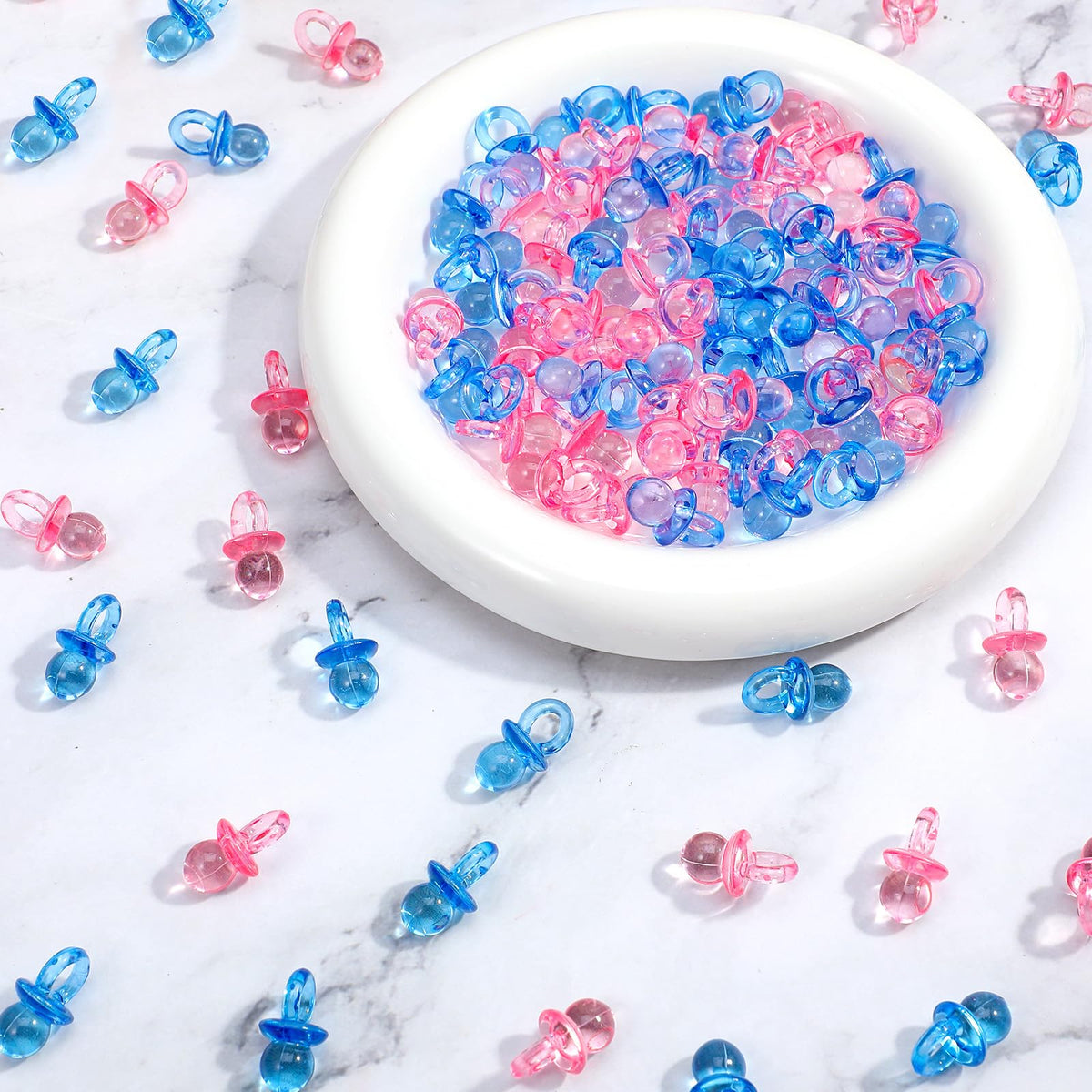 XLIUAX 100-pack mini acrylic pacifiers in blue and pink for colorful baby shower decor and gender reveal ideas.